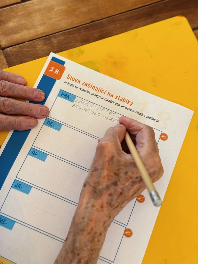 Seniorka tužkou doplňuje slova do pracovního listu