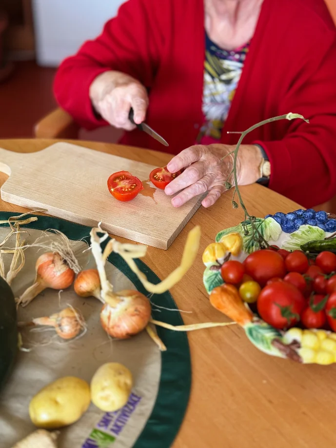 Seniorka krájí cherry rajčata, vedle leží cibule a brambory