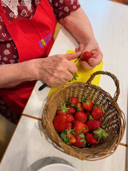 Seniorka čistí jahody nad košíkem plným jahod