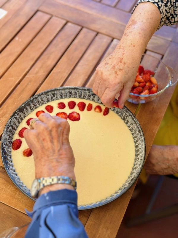 Ruce seniorky skládají jahody na koláč s krémovou náplní